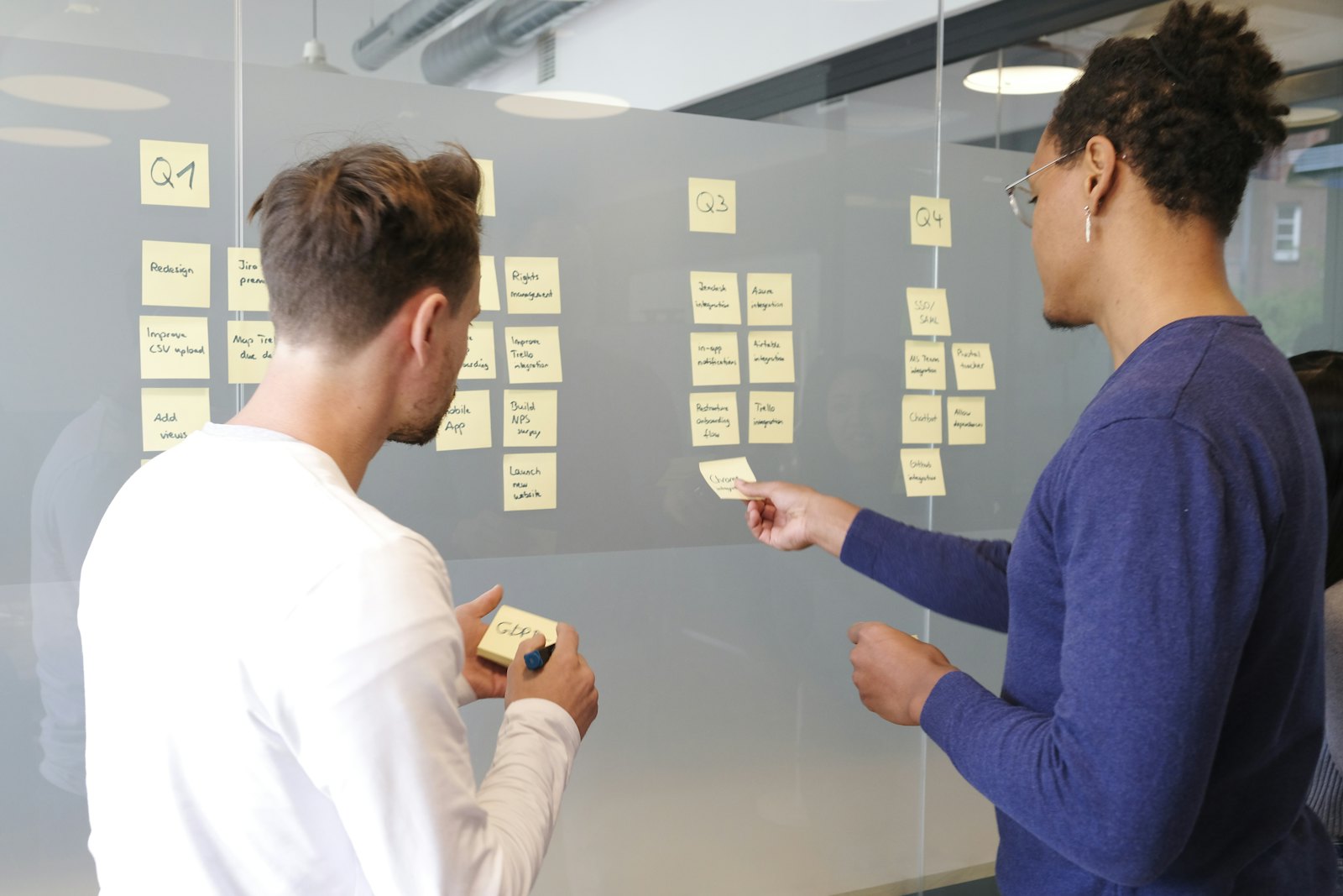 Two people arranging sticky notes on a glass wall